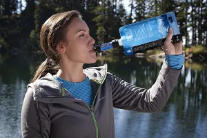 Woman using a Sawyer Mini Water Filter in front of a lake